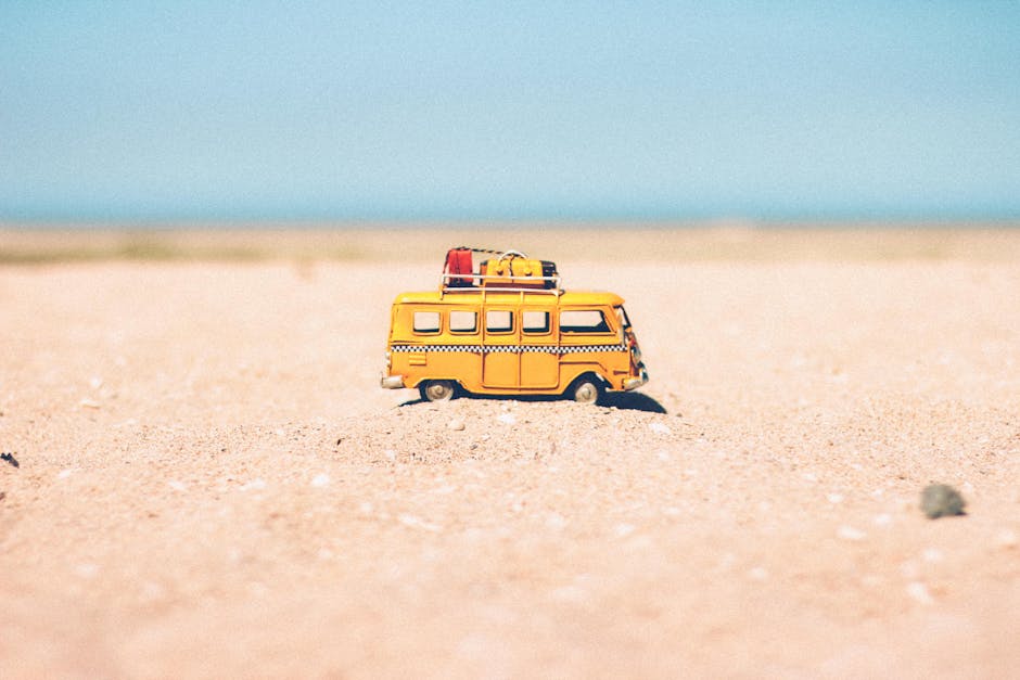 A toy van on a sandy beach evokes summer travel and vacation vibes
