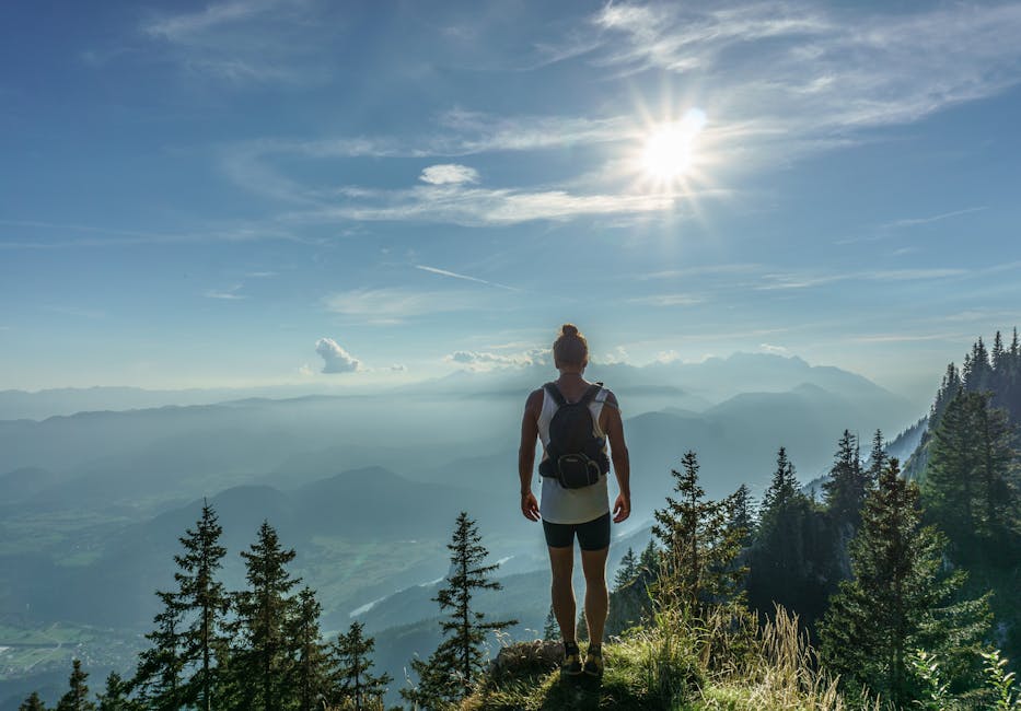 A lone hiker stands on a mountain top, overlooking a breathtaking landscape in Slovenia under the bright sun